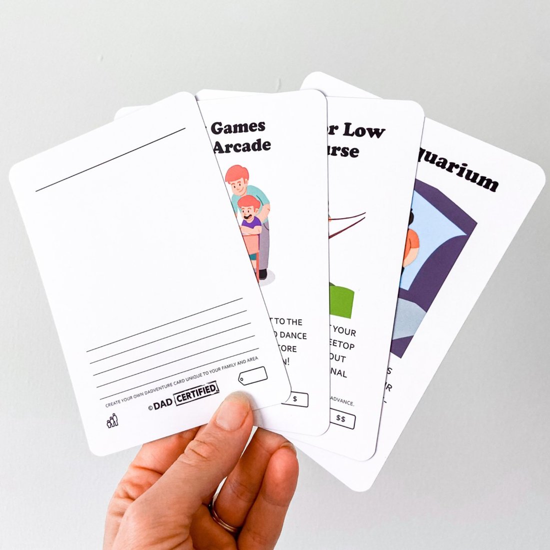 A hand holding Dadventure cards fanned out, including a blank create-your-own card